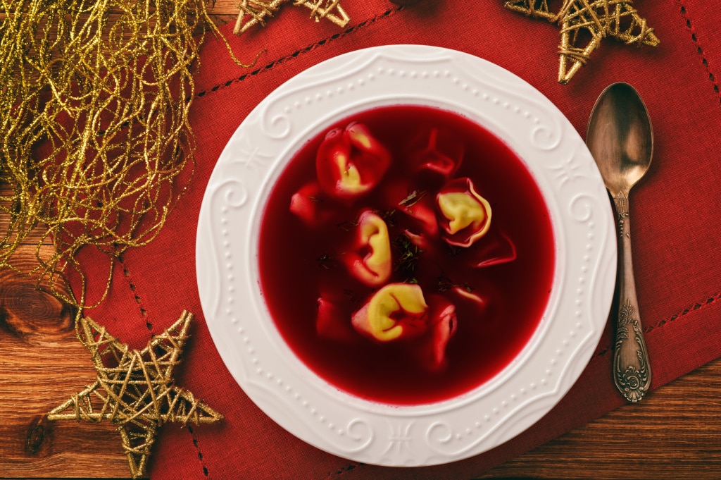Traditional Polish christmas soup - red borscht soup with dumplings on white plate.