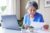 Seniorka siedząca przed laptopem i czytająca rachunek.